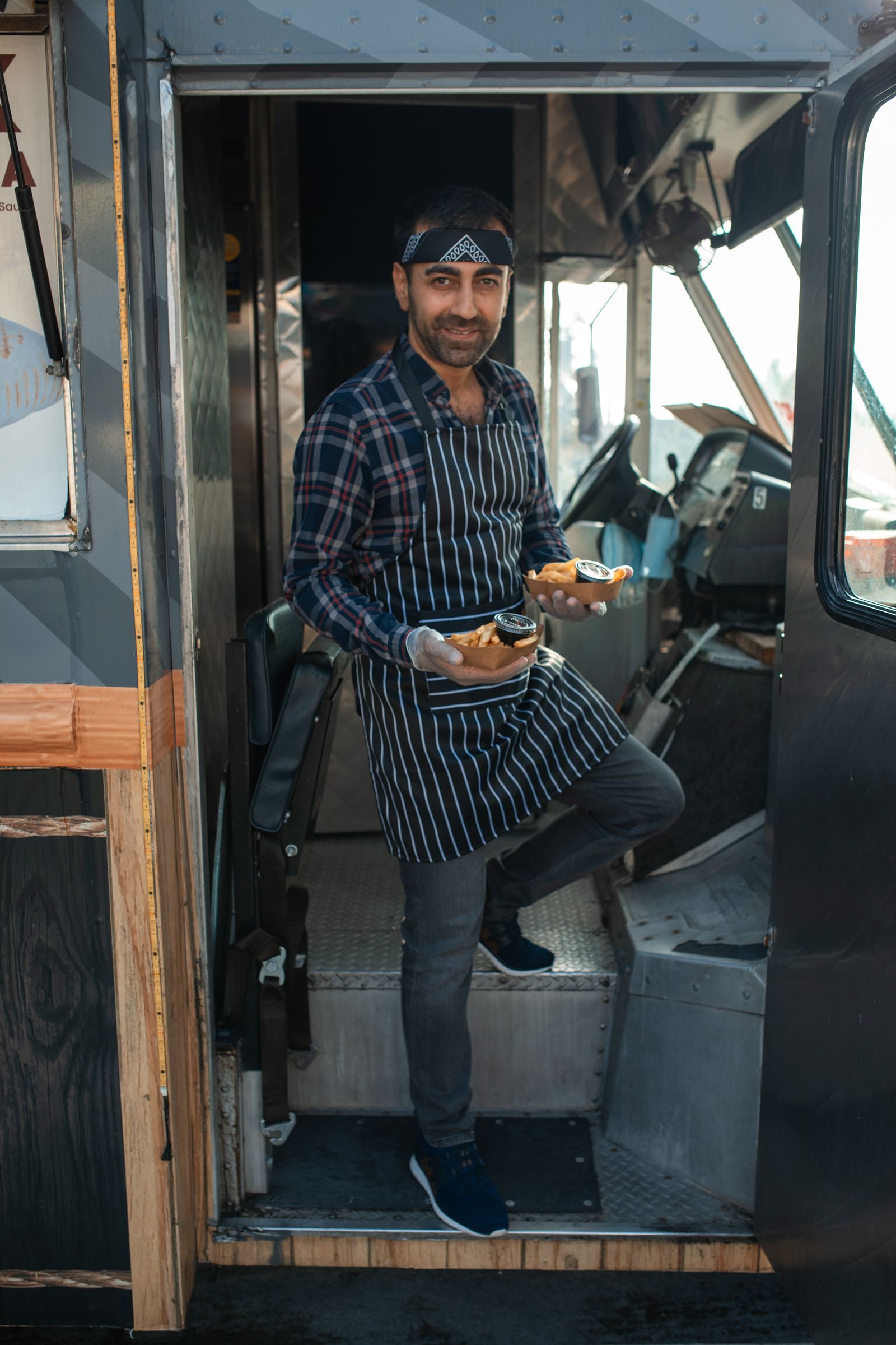 A food truck owner serving prepared food orders at the truck window.