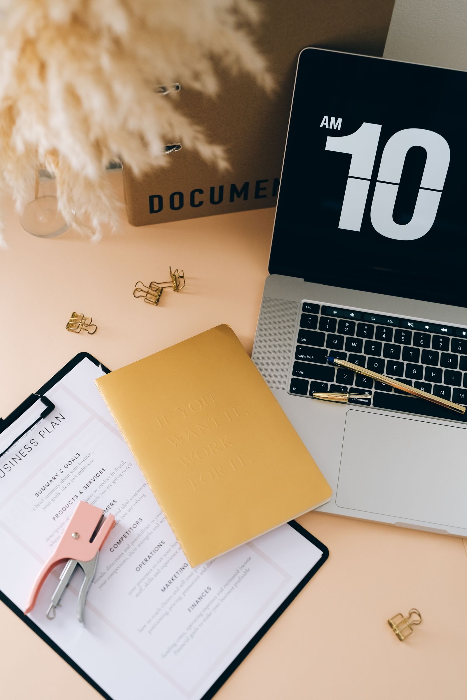 A business planning notebook, laptop, and stationery arranged on a desk.