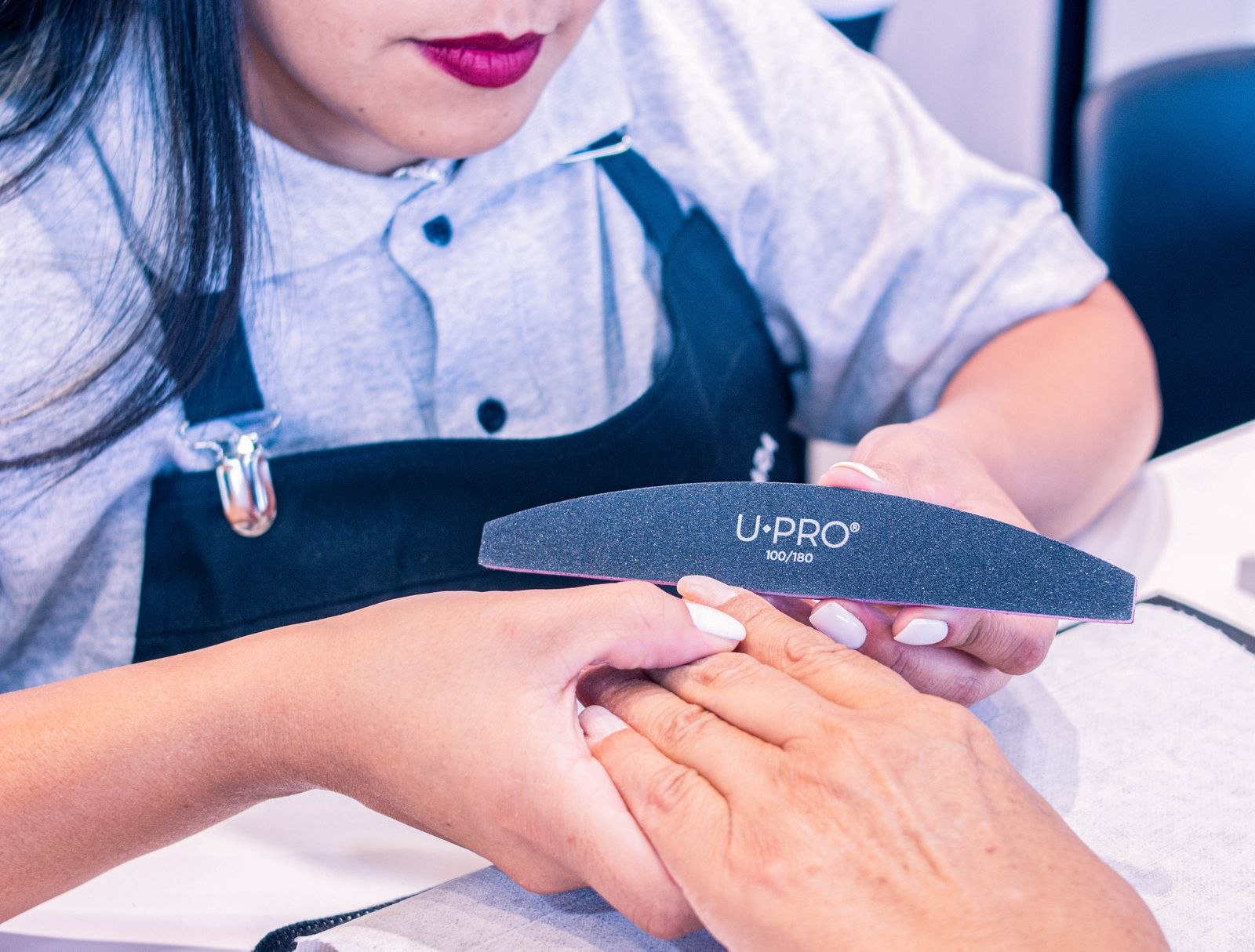 A nail technician working on a customer's manicure at a salon table.