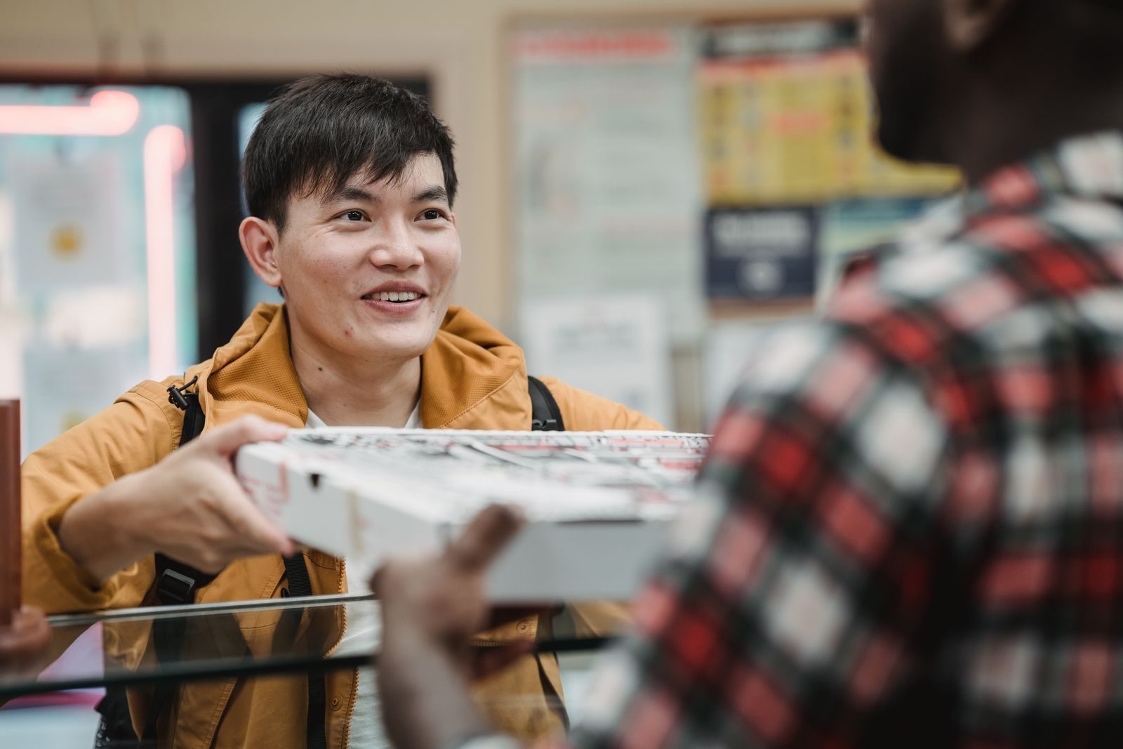 A customer receiving a boxed pizza from a pizza shop employee.