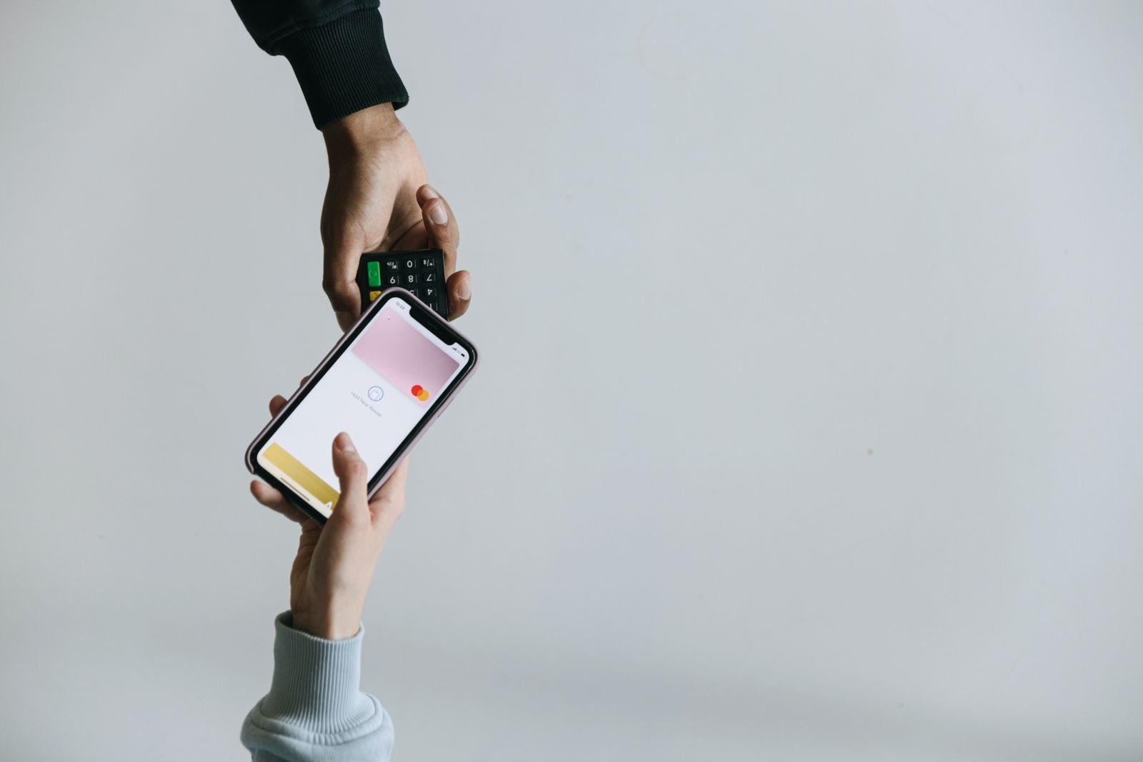 A customer holds a smartphone beside a payment terminal at checkout.