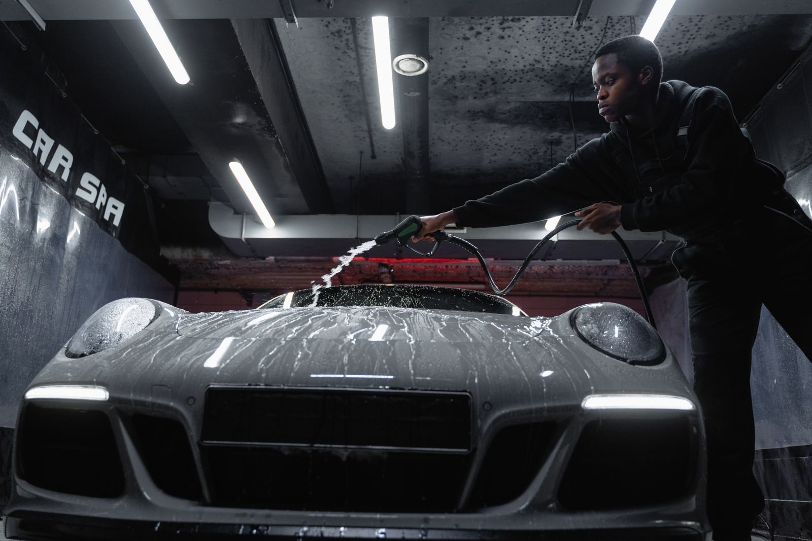 A car wash professional rinsing a car inside an indoor wash bay.